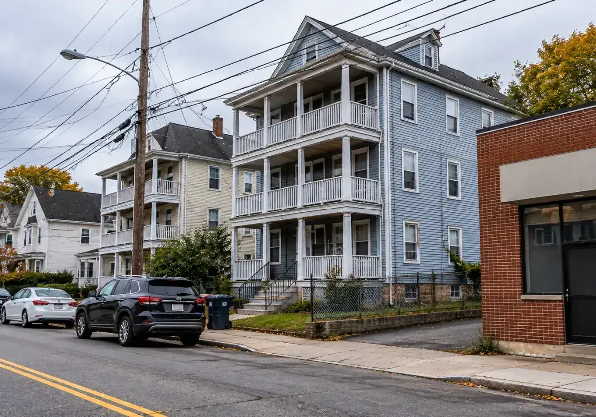 Blue triple-decker home with stacked porches next to a small brick commercial building in East Woburn, MA